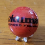 Okuma Fishing Reels Marble Rods Tackle Advertising 1" Shooter Sz Stand. Fixed Price $13.99.